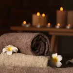 Zusammengerollte Handtücher mit weißen Blumen in einer warmen, kerzenbeleuchteten Spa-Atmosphäre.
